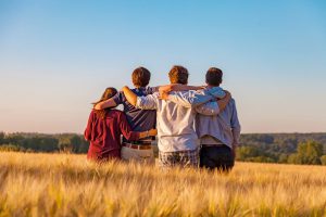 Young friends, arms around each other's shoulders, standing in field.