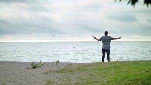 Man with Bible in hand and his arms raised, on the beach and looking towards the sky.